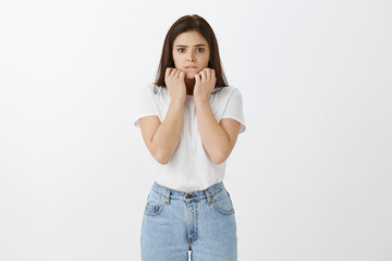 Worried intense cute caucasian woman in trendy jeans and t-shirt, clenching fists near face and...