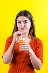 Beautiful happy girl with orange juice on yellow background