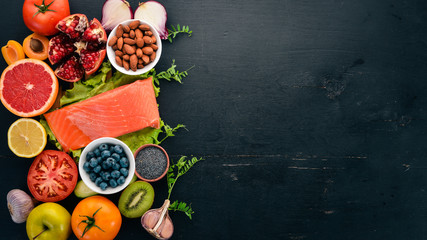 A set of healthy food. Fish, nuts, protein, berries, vegetables and fruits. On a black wooden...