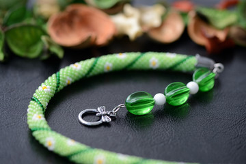Green summer necklace with chamomile print on a dark background close up