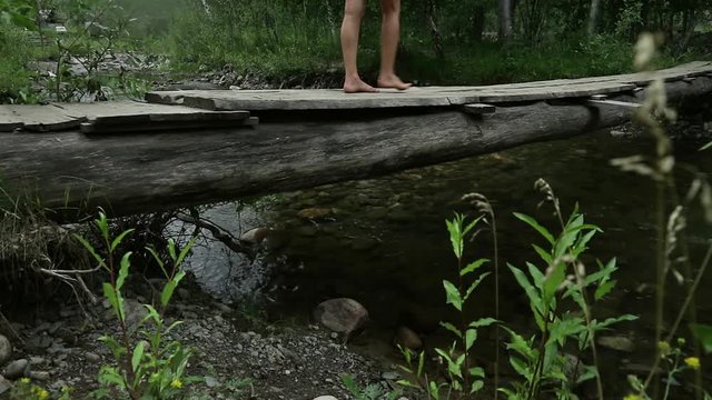 young woman are walking along a narrow wooden bridge over a mountain river. camping and adventure concept
