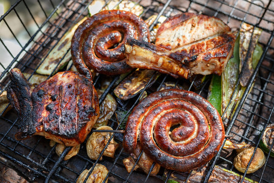 Twisted sausages, pork steak, mushrooms and zucchini cooked on grill.