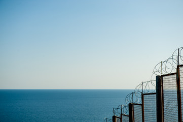 barbed razor fencing on state border against illegal immigration near sea sky - obrazy, fototapety, plakaty