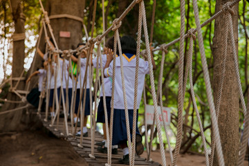 Fototapeta premium Cute student child girl walking on the hanging rope bridge across the river in the forest with fun