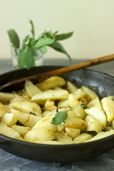 Young fried potatoes with onions and sage in a frying pan on a concrete table.