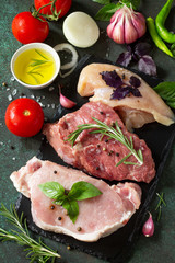 Fresh raw meat. Different types of raw pork meat, chicken fillet and beef with vegetables and herbs on dark wooden background.