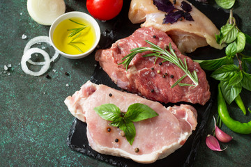 Fresh raw meat. Different types of raw pork meat, chicken fillet and beef with vegetables and herbs on dark wooden background. Copy space.