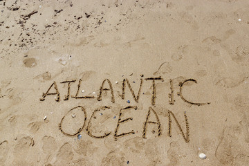 Lettering Atlantic ocean written on the beach. Writing on the wet sand. Vacation and tourism concept.