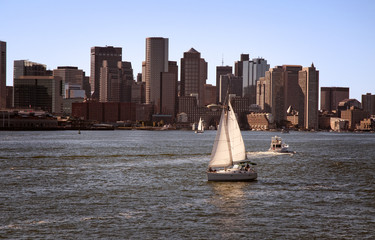 Sailboat in Boston Harbor with Skyline of Buildings Along the Shore as Sun Sets