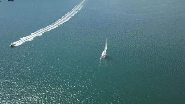 Flying over sail boat and speed boat. Sky view of boats on ocean in England.