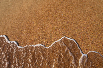 Fototapeta na wymiar Spuming sea water surfing on brown sand sunset background
