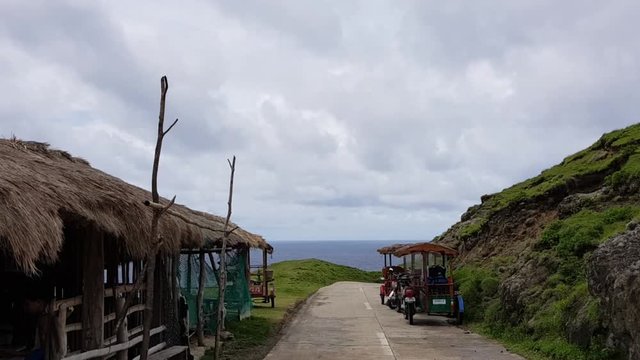 Fast moving clouds above a road with a nearby hut and tricycle.