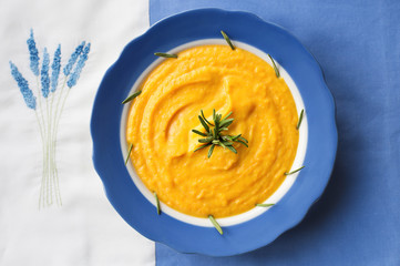 pumpkin soup in a blue plate with rosemary on a napkin with flowers