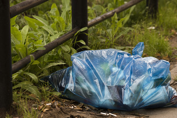 Blue bag with trash and cigarette butts near the fence