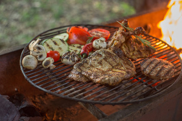 Grilled meats and vegetables on the grill, fire in the background