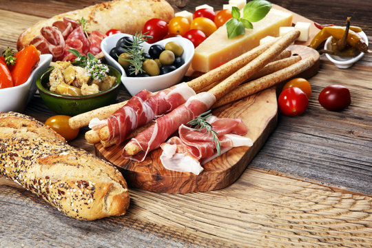 Italian antipasti wine snacks set. Cheese variety, Mediterranean olives, crudo, Prosciutto di Parma, salami and wine in glasses over wooden grunge background.