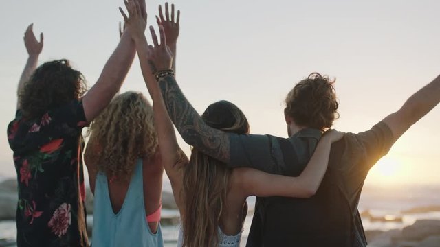 group of friends embracing on beach celebrating with arms raised at sunset