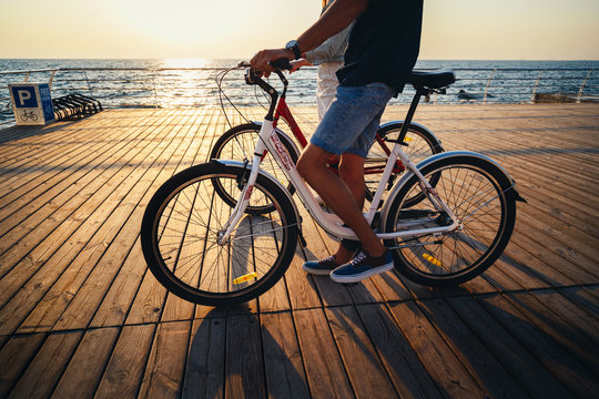 Close up of couple of young hipsters cycling together at the beach at sunrise sky at wooden deck summer time