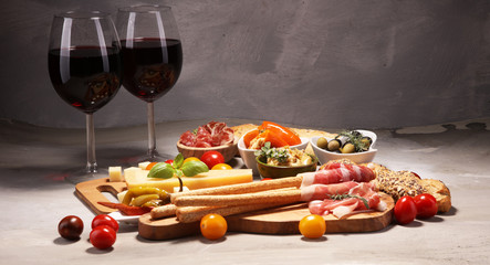 Italian antipasti wine snacks set. Cheese variety, Mediterranean olives, crudo, Prosciutto di Parma, salami and wine in glasses over stone grunge background.