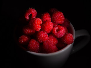 Raspberry in a mug on a black background.