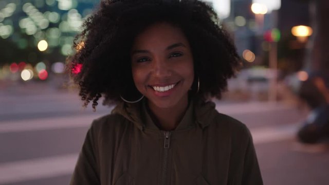 portrait of stylish young african american woman with afro smiling happy at camera enjoying night life in urban city