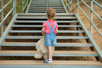 little girl climbs up the stairs with a soft toy in her hands. Movement up, development, recovery