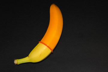 yellow banana and orange condom on a black background