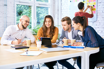 Group of students looking at tablet while studying together in university. Young creative workers brainstorming during meeting
