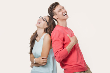 Happy young lovely couple standing back to back and laughing over white background. Friendship and relationships
