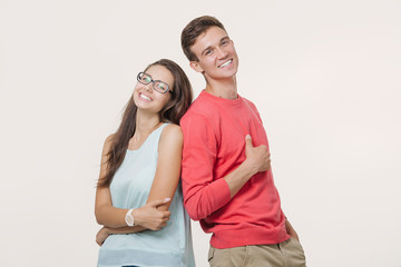 Happy young lovely couple standing back to back and smiling looking at camera on white background