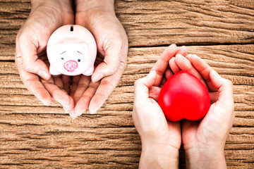 Man and women hand hold a piggy bank and red heart with copy space on old wood background, Health...