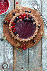 Raw vegan pie with berry jam and organic currants on blue background copyspace