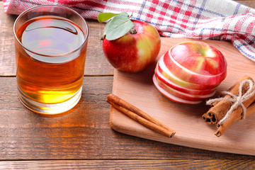 Apple juice with fresh ripe apples and cinnamon sticks on a brown wooden background