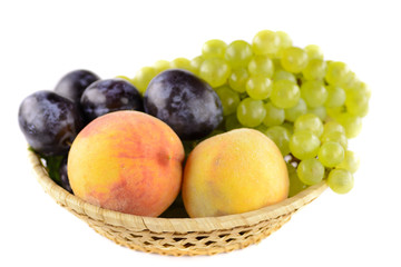 A bowl of tasty, ripe summer fruits with white background. In the bowl peach, plum and white grapes.