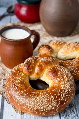 Fresh ruddy round bagels with sesame and milk in a clay mug on an old wooden table.