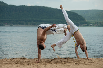 Men train capoeira on the beach - concept about people, lifestyle and sport.