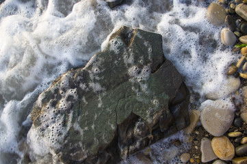 pebble stones on the sea beach, the rolling waves of the sea with foam