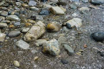 pebble stones on the sea beach, the rolling waves of the sea with foam