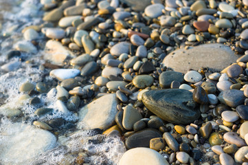 pebble stones on the sea beach, the rolling waves of the sea with foam