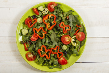 Vegetable salad with fresh tamata vegetables, cucumbers, lettuce, onions and arugula on a wooden table in a glass bowl. Vegetarian food salad. The concept of a healthy diet
