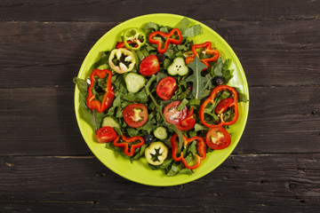 Vegetable salad with fresh tamata vegetables, cucumbers, lettuce, onions and arugula on a wooden table in a glass bowl. Vegetarian food salad. The concept of a healthy diet
