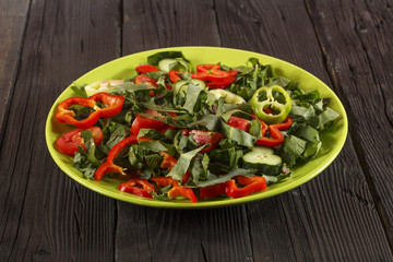 Vegetable salad with fresh tamata vegetables, cucumbers, lettuce, onions and arugula on a wooden table in a glass bowl. Vegetarian food salad. The concept of a healthy diet
