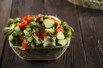 Vegetable salad with fresh tamata vegetables, cucumbers, lettuce, onions and arugula on a wooden table in a glass bowl. Vegetarian food salad. The concept of a healthy diet
