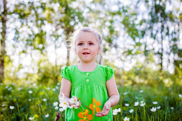little girl in a green dress in a clearing in the summer with flowers