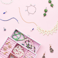 Open jewelry box with neclaces, earrings and rings on pastel background. Top view