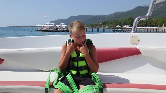 Brave kid sitting in motorboat ready for parasailing flight over summer beach. Family has fun during vacation. Real time full hd video footage.