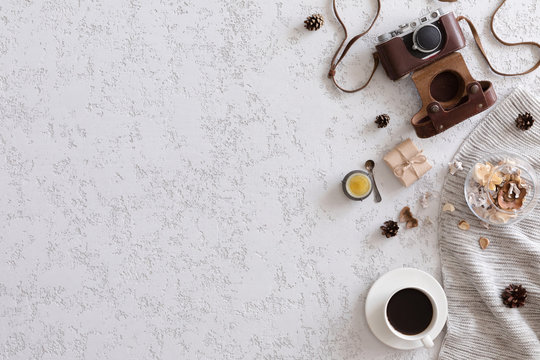 Winter flat lay background. Top view of workspace or office desk with laptop, vintage photo camera, blanket, cup of coffee, ginger cookies, cone on textured white background