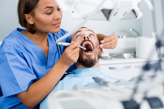 doctor woman in uniform is examinating of man on the chair in the dental office