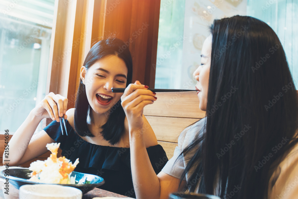 Wall mural two young attractive asian women eating shrimp tempura japanese food at restaurant with happiness an