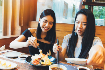 Two young attractive Asian women eating Shrimp Tempura Japanese food at restaurant with happiness...
